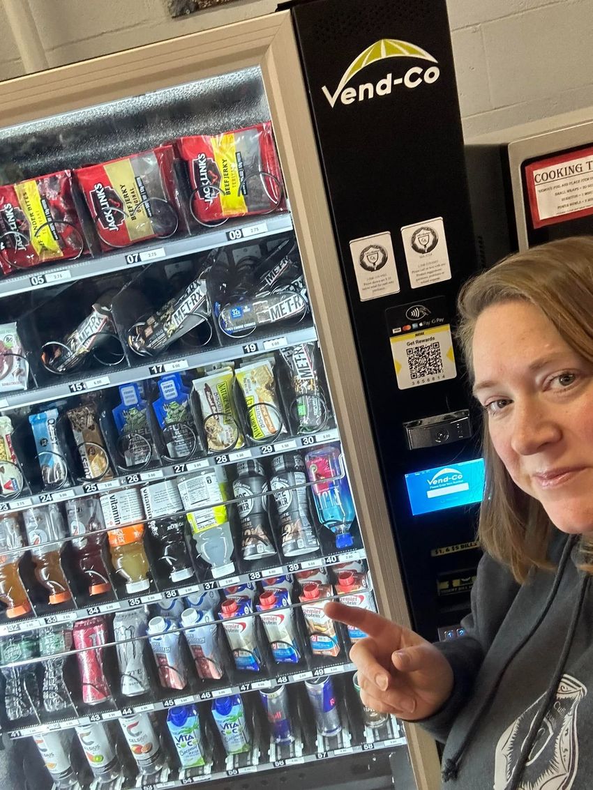 Woman pointing at a vending machine stocked with drinks in a convenience store.