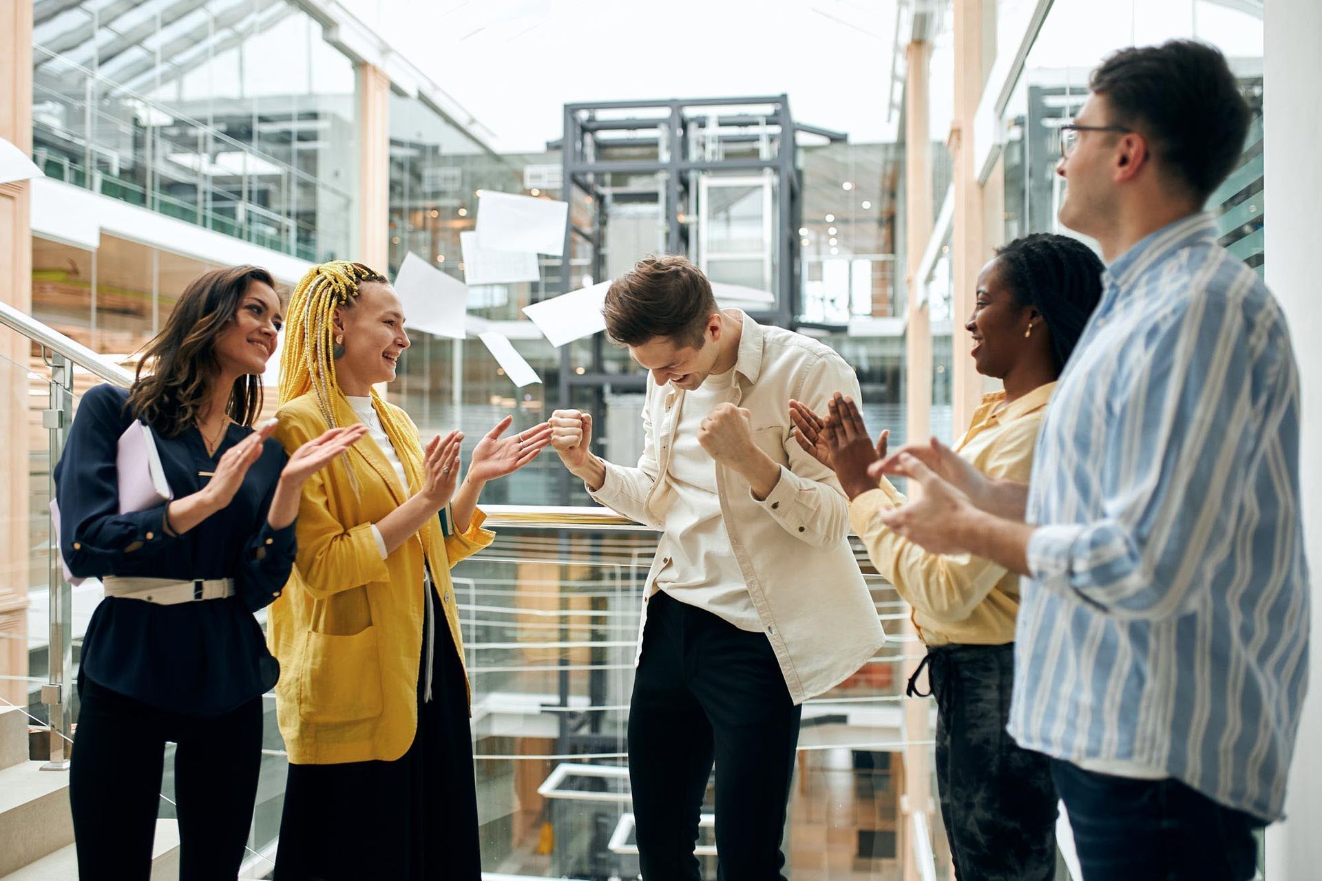 Five coworkers chatting and laughing in a bright modern office hallway