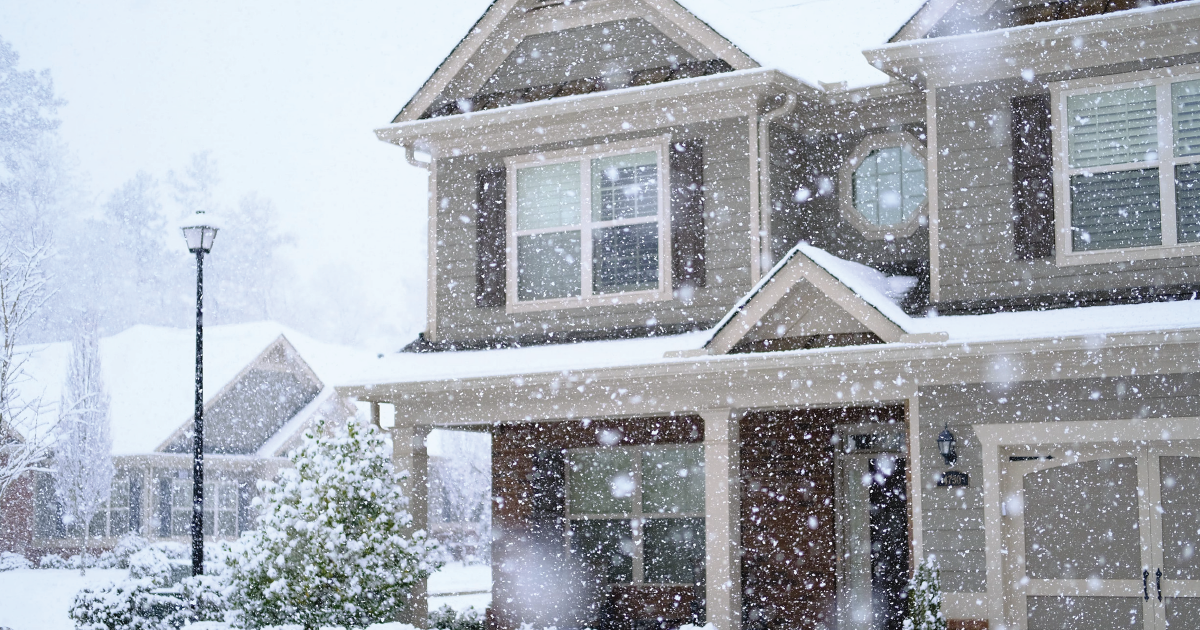 Snowy suburban house with a porch and front yard during a heavy snowfall