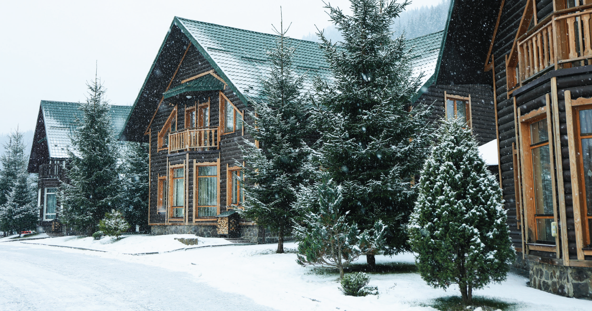 Snow-covered log cabins and evergreen trees in a winter village scene