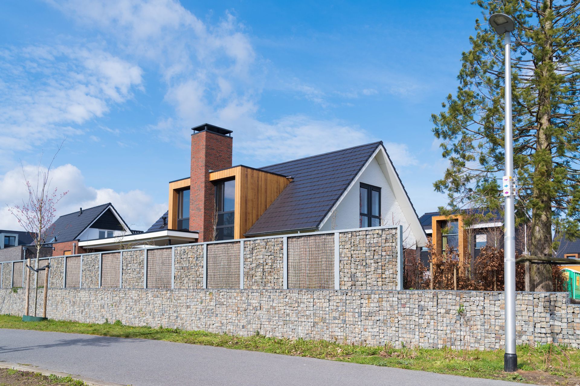Modern house with a stone wall, blue sky, and trees along a quiet street