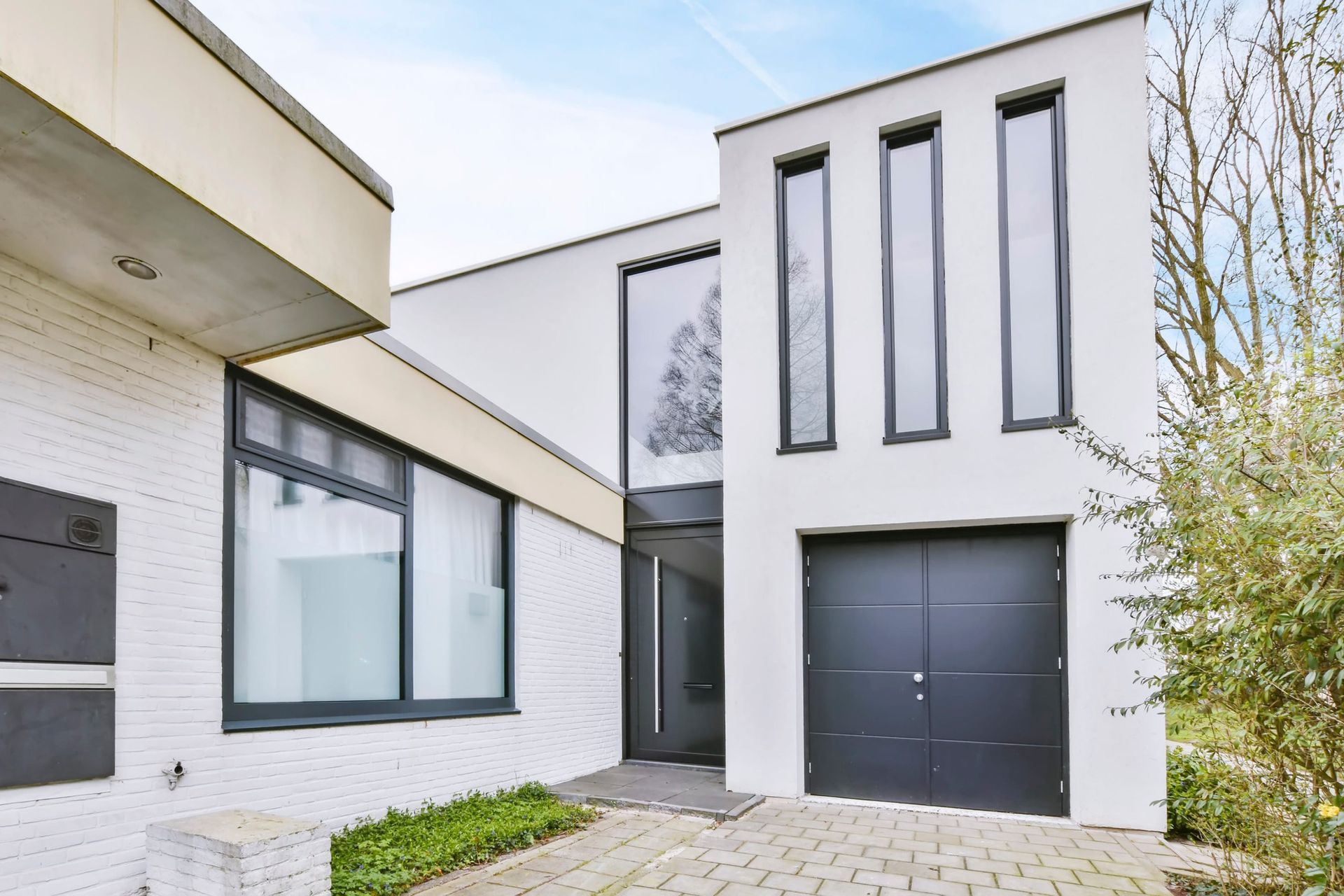 Modern white house facade with large windows, black double door, and paved driveway