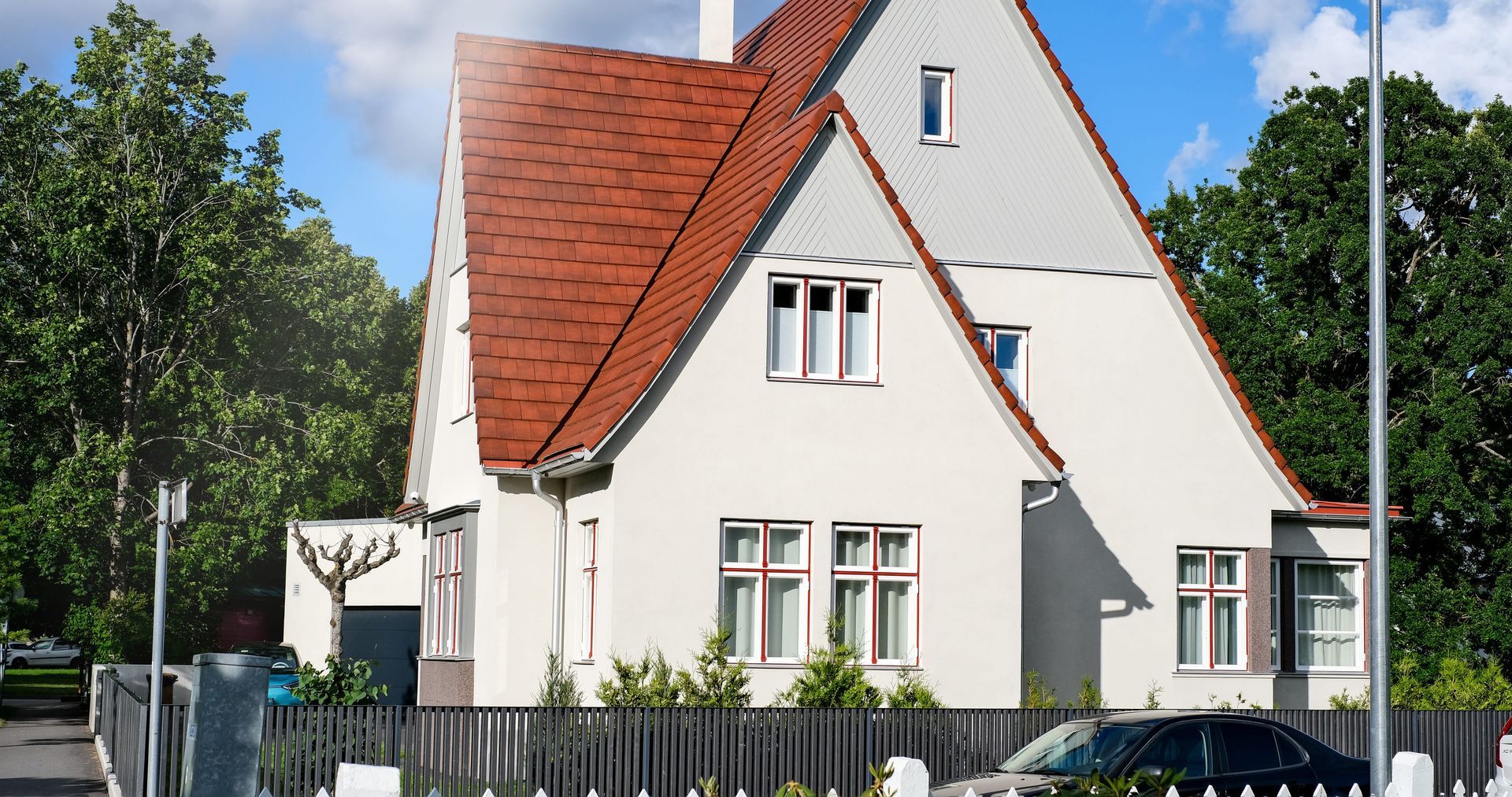 White house with a red tiled roof and fence, surrounded by trees on a sunny day