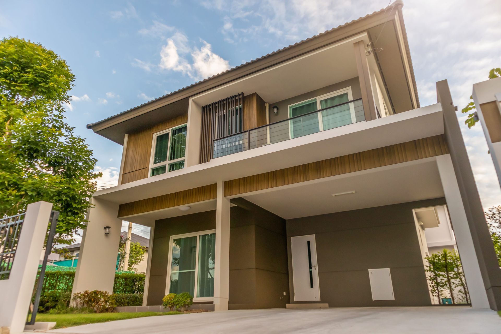 Modern two-story house with a carport, balcony, and large windows under a bright blue sky