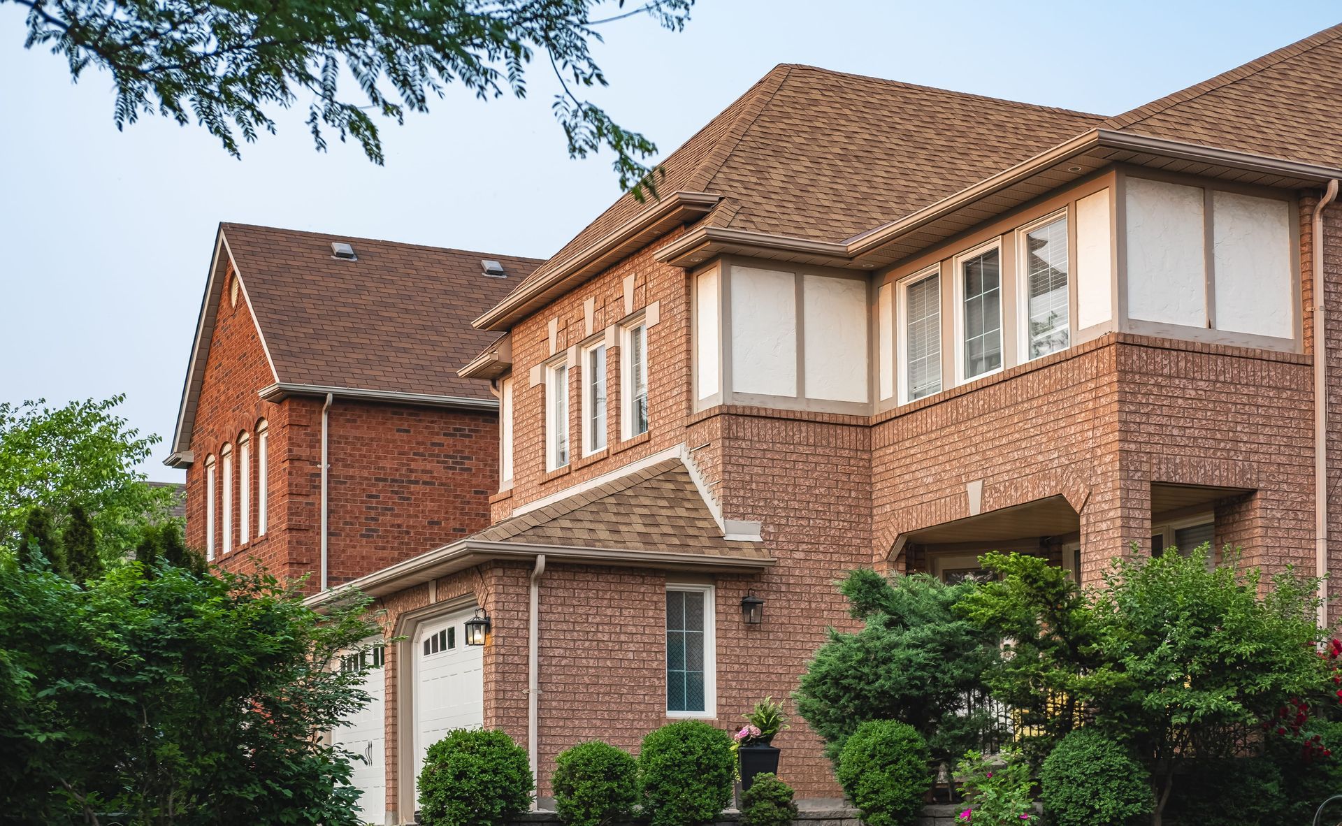 Brick suburban houses with brown tiled roofs and green shrubs under a clear sky