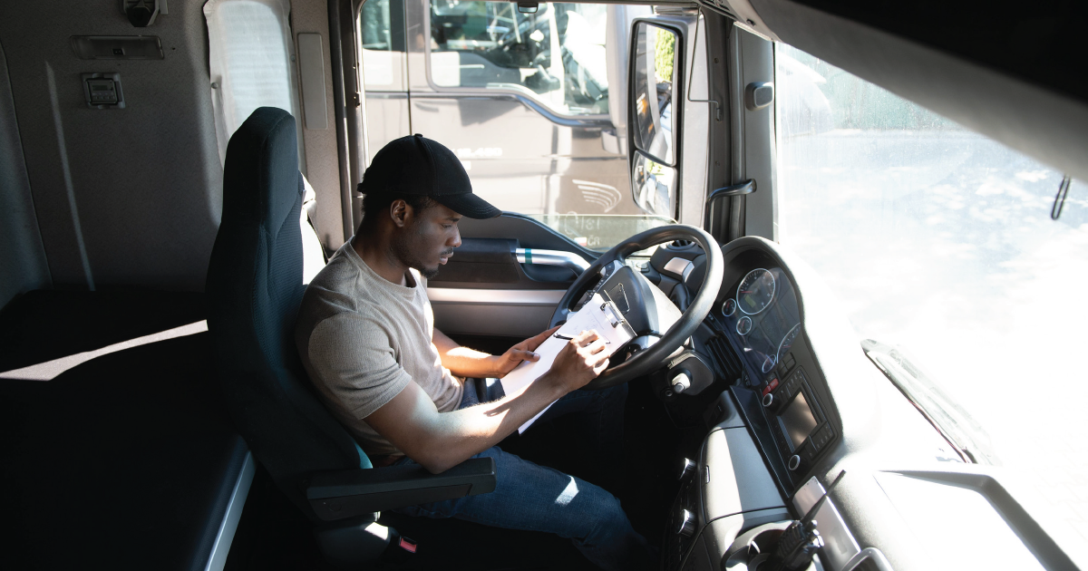 Person sitting in a truck cab, looking at a phone while holding the steering wheel