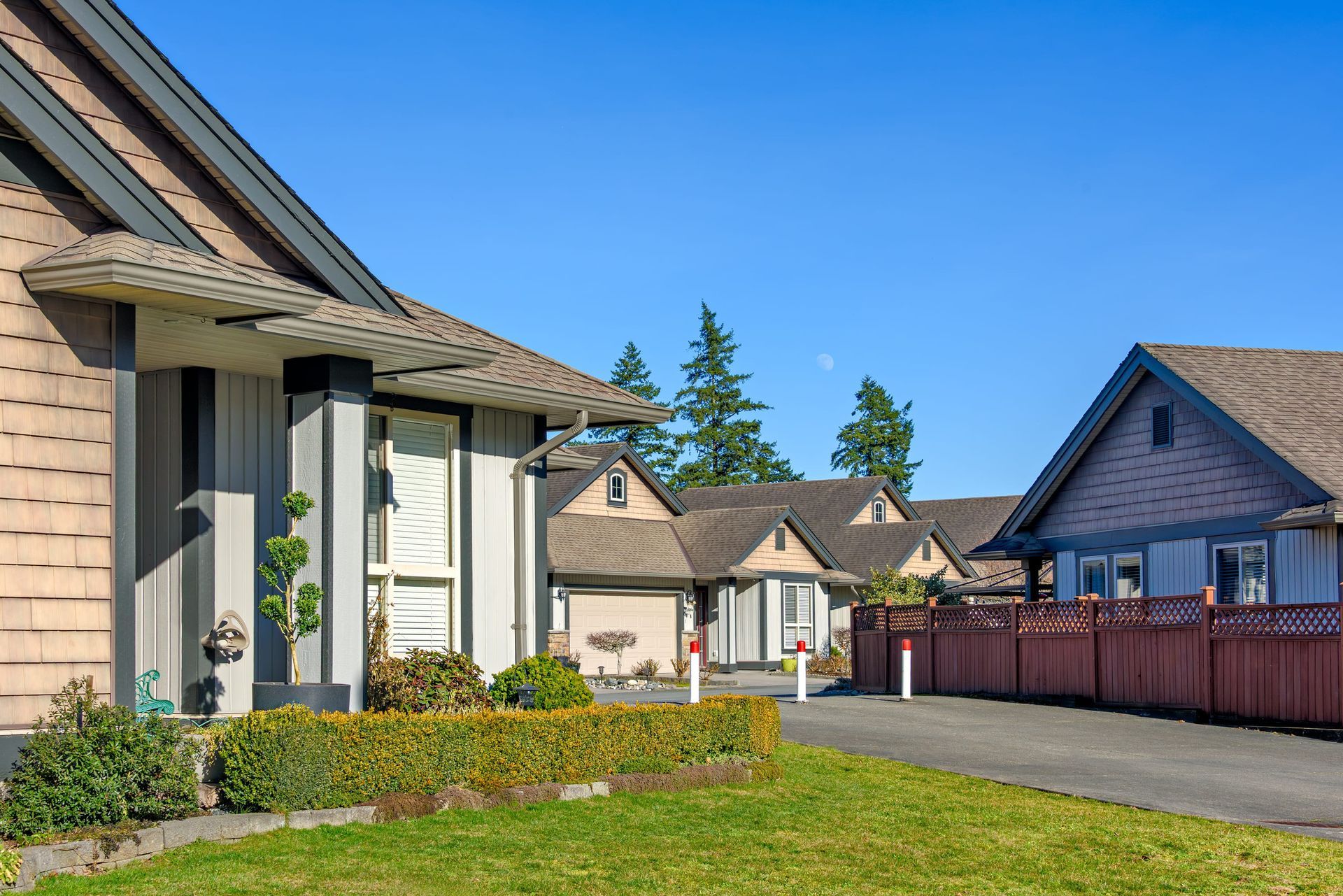 Suburban house with landscaped yard, white garage, and red fence under a clear blue sky
