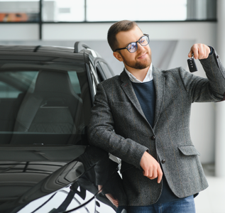 Man leaning on a black car and holding up a key fob in a showroom