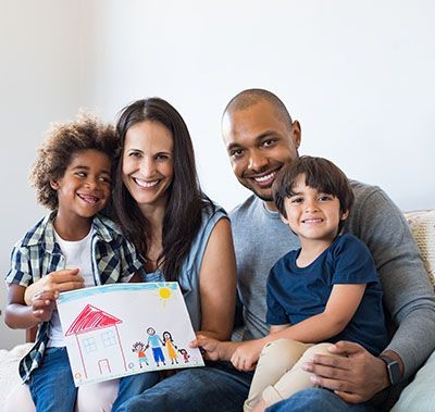 Family playing together in a bright living room, with a child on a man's shoulders and a woman behind them.