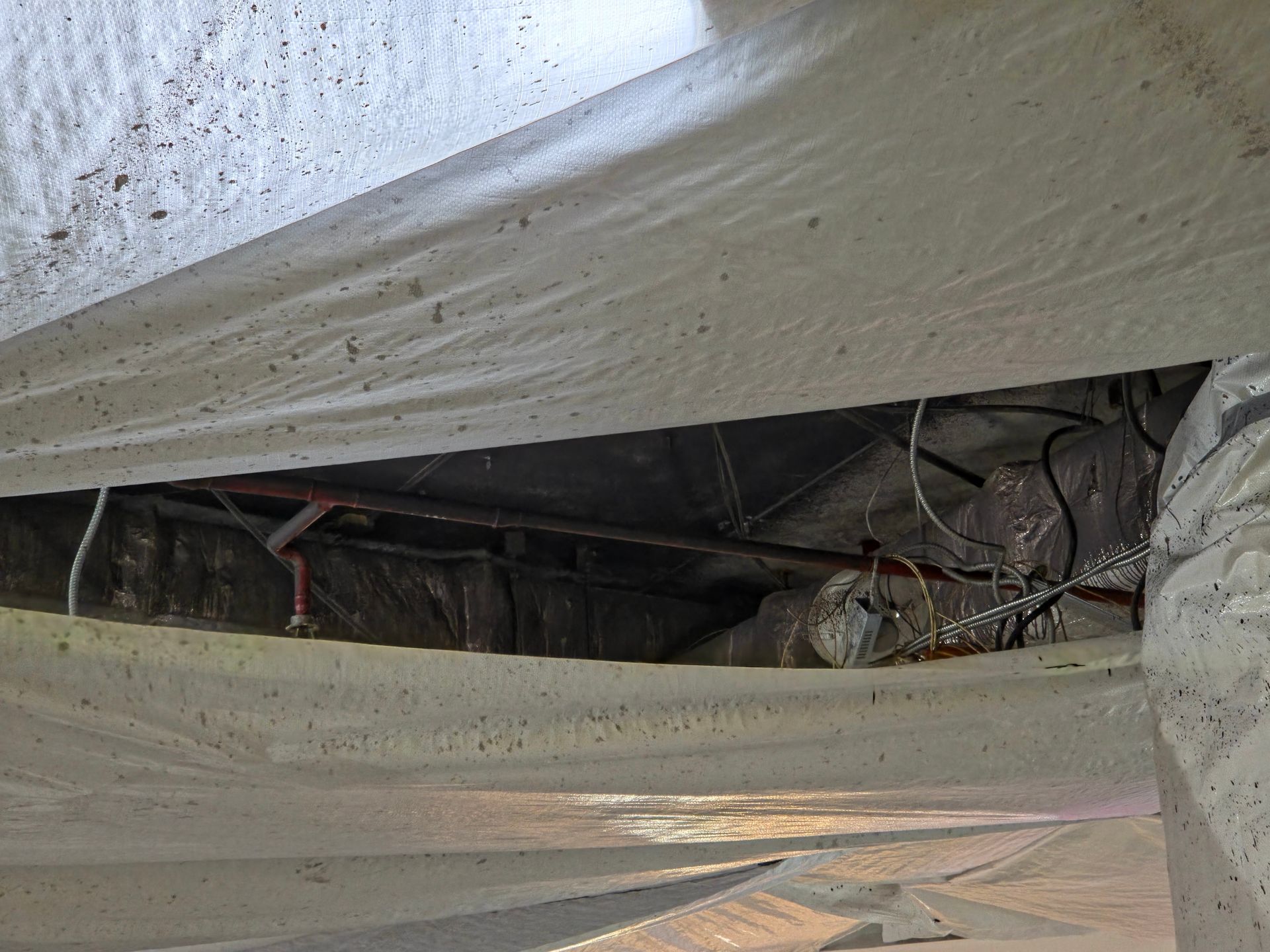 Torn white tarps exposing wires and a dark interior in a damaged structure