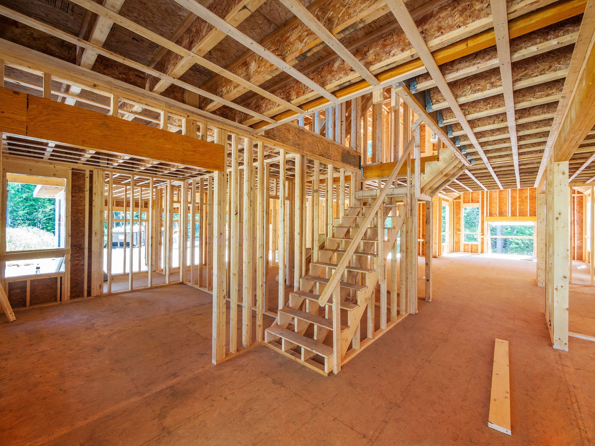 Interior of a house under construction with exposed wooden framing, stairs, and unfinished floors