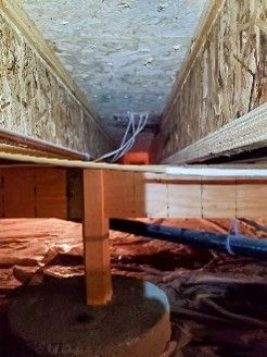 a narrow crawlspace beneath a floor with wooden beams and a concrete support pillar.