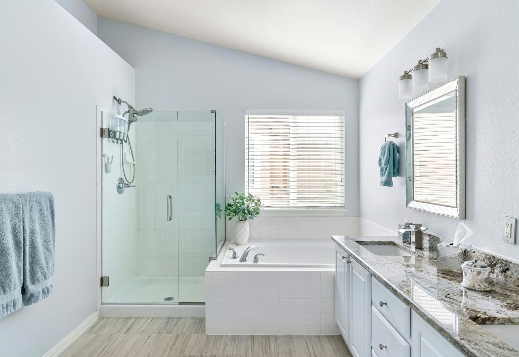 Bright modern bathroom with glass shower, soaking tub, double vanity, and window blinds