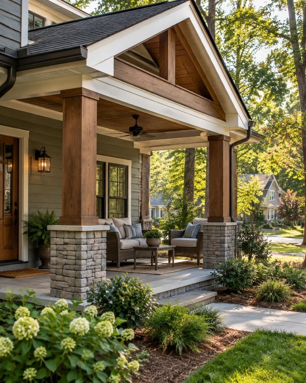 Covered front porch with stone columns, outdoor seating, and lush landscaping on a sunny house exterior.