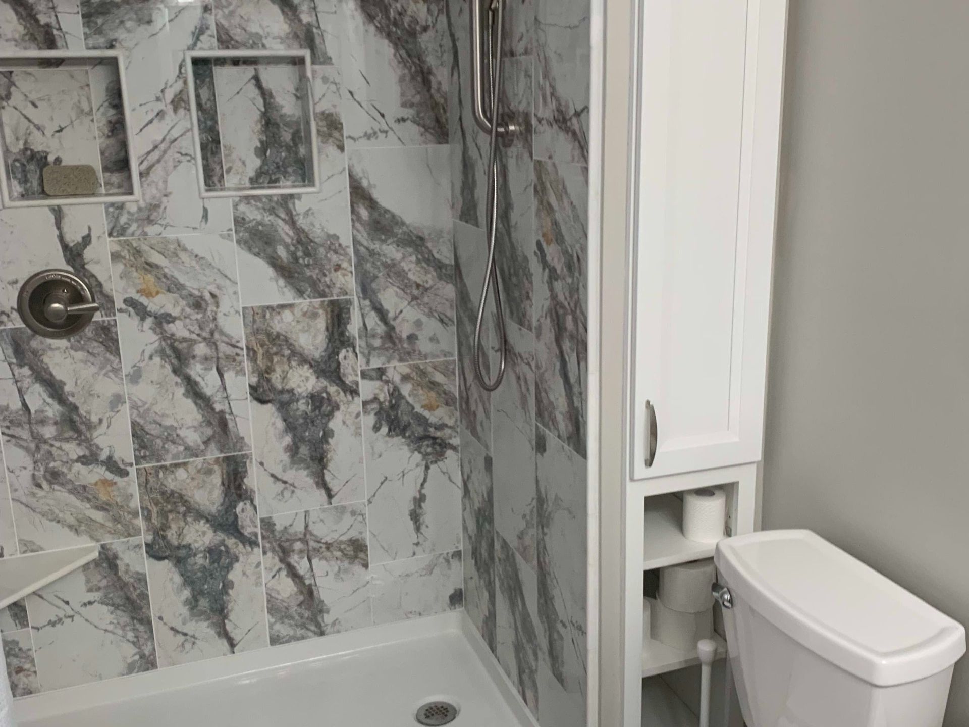 Bathroom with marble tile shower and white toilet next to a built-in cabinet.
