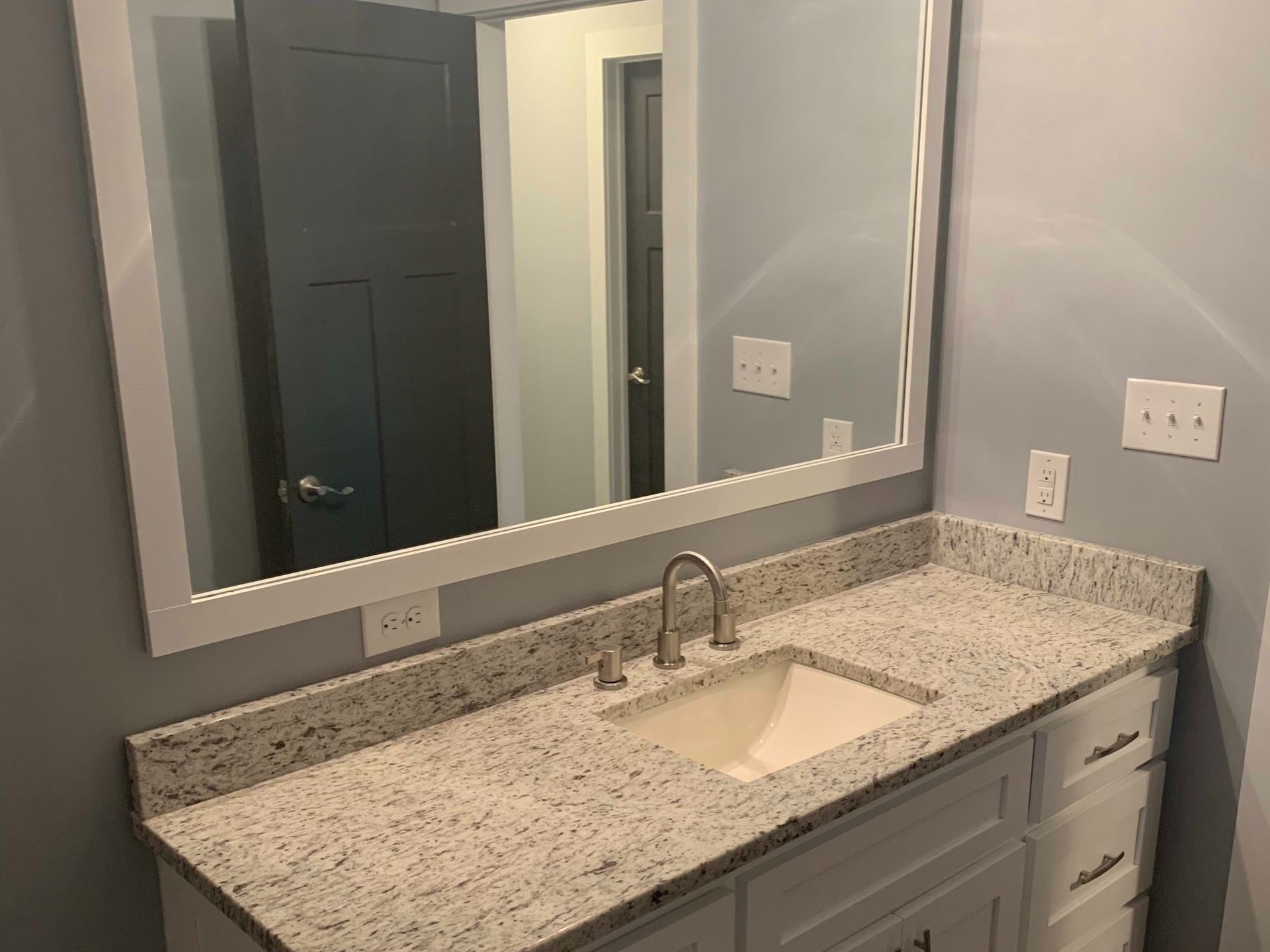 Modern bathroom vanity with speckled granite countertop, undermount sink, mirror, and gray walls