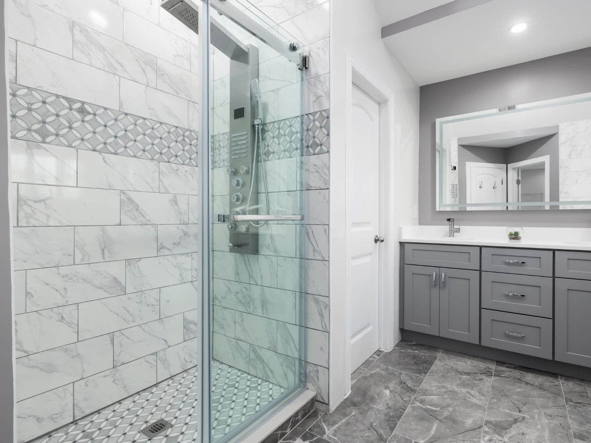 Modern bathroom with glass shower, gray vanity, large mirror, and marble-patterned tile floor