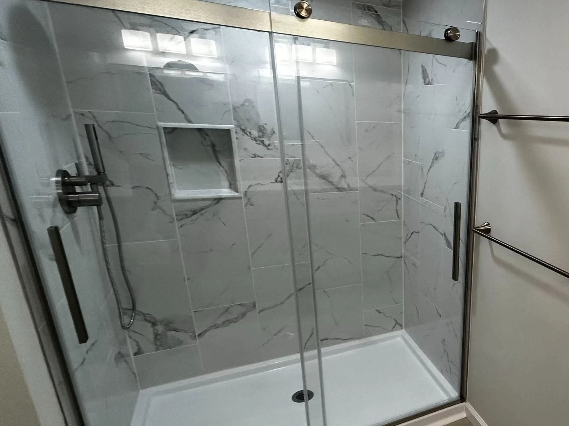 Glass walk-in shower with marble-look tile, black hardware, and a built-in shelf.