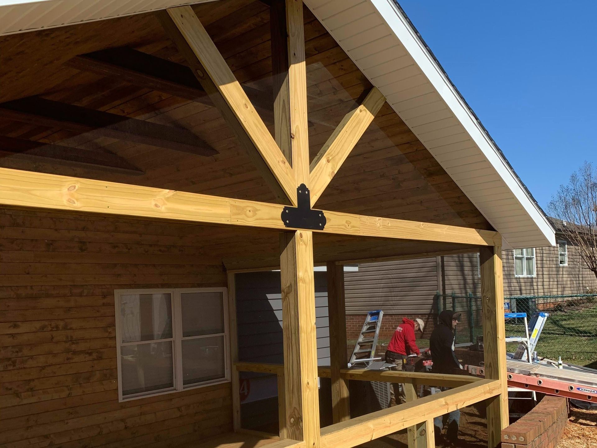 Wooden porch under construction with exposed beams and workers near the house exterior