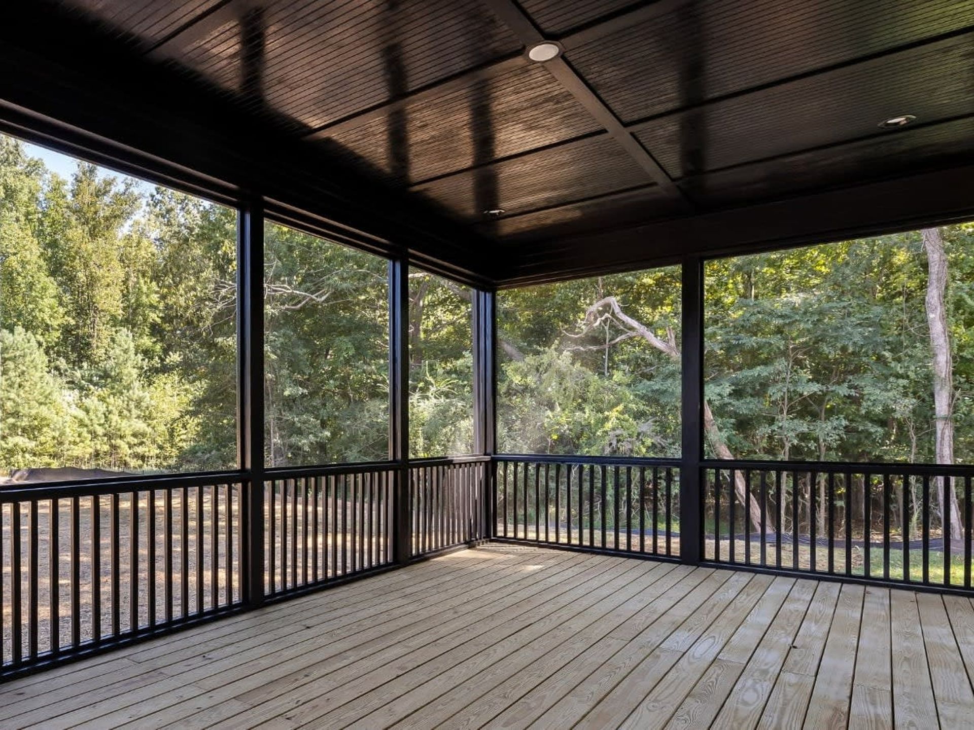 Covered wooden deck with black railings overlooking trees and woods
