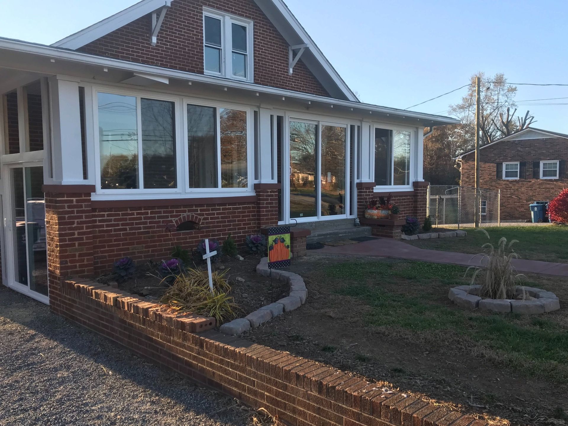 Brick house with white-trim windows, front garden, and curved brick retaining wall in a sunny yard.