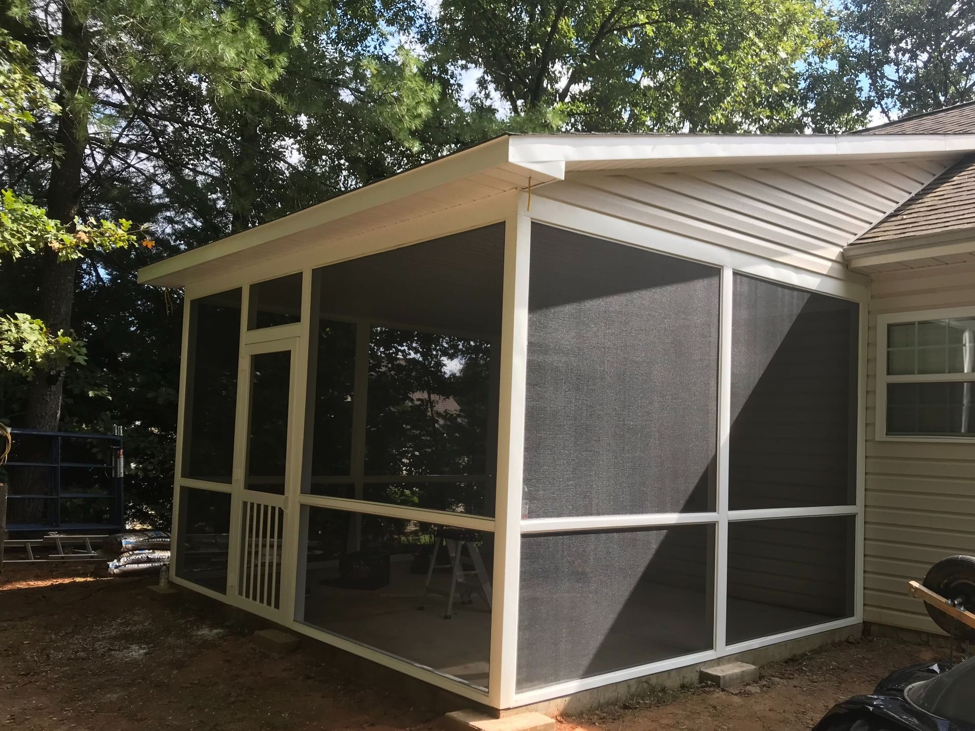 Screened porch addition with white trim and gray mesh panels beside a house in a wooded yard