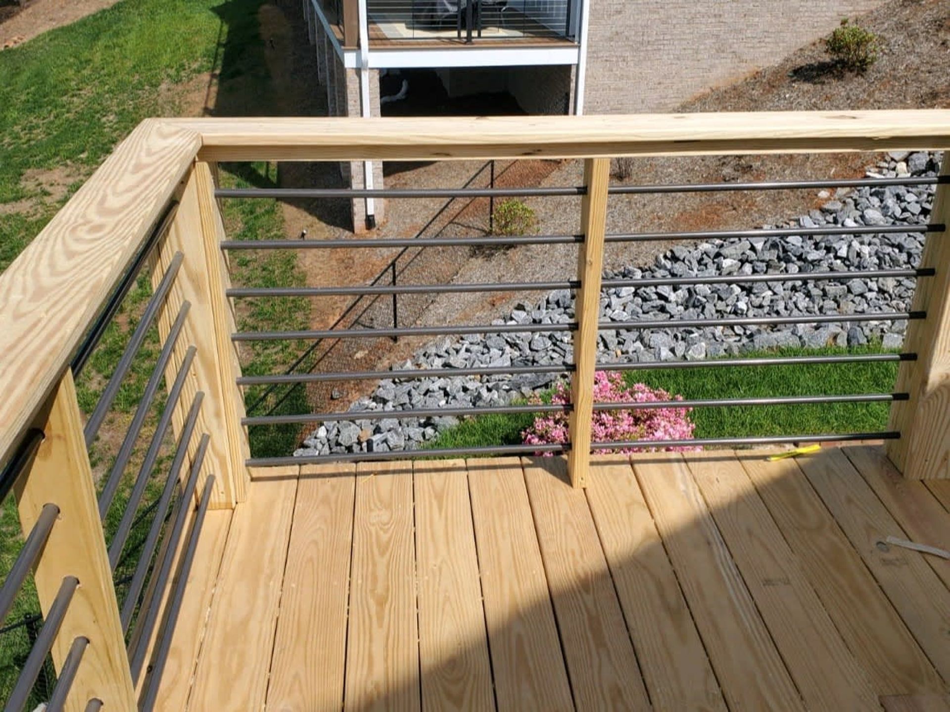 Wooden deck with metal railing overlooking a landscaped yard and gravel path