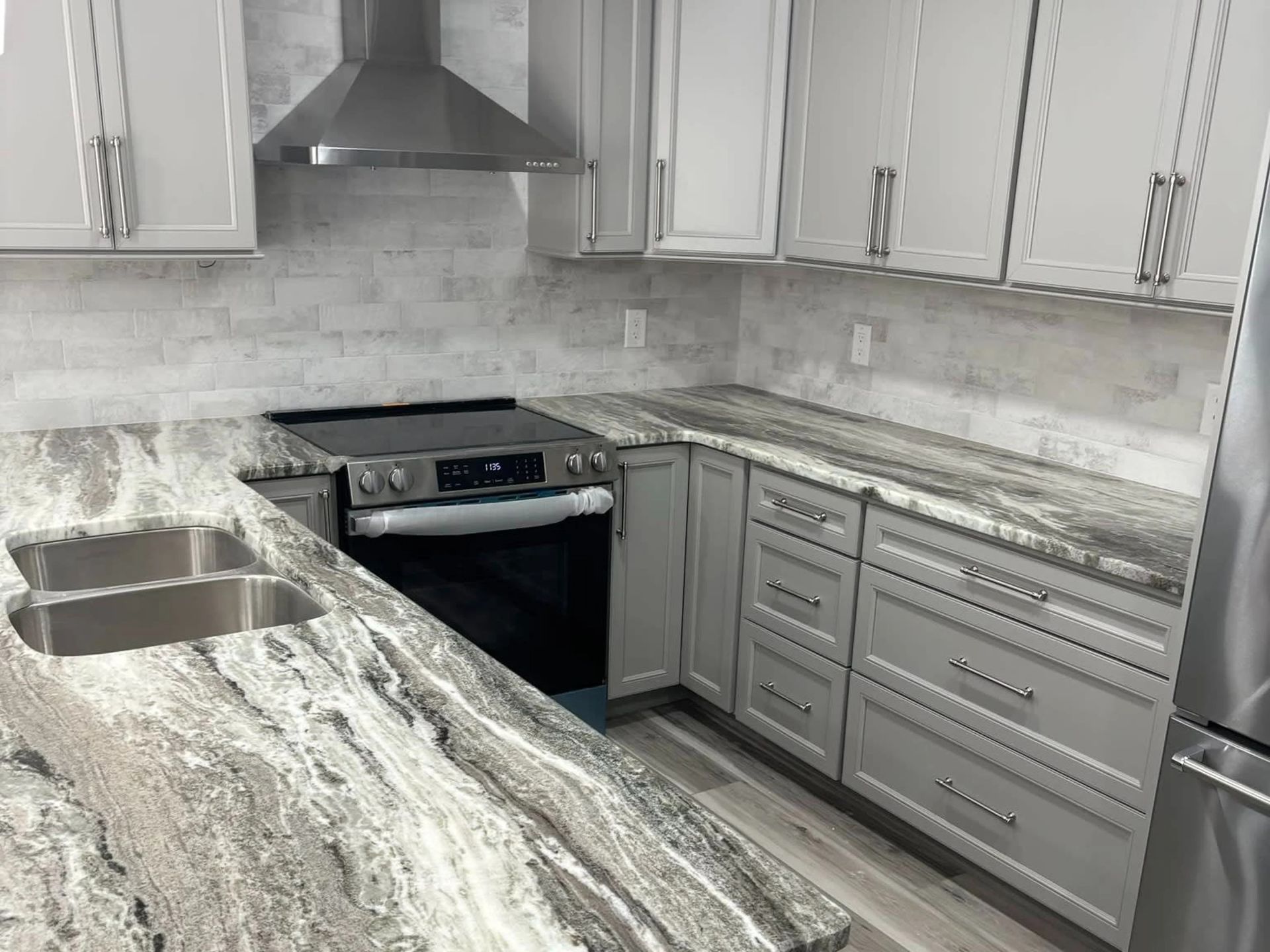 Modern kitchen with white cabinets, gray marble-look countertops, stainless steel range hood, and black stove