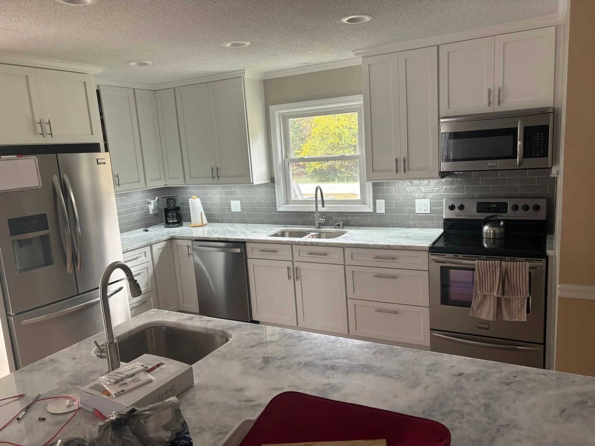 Bright modern kitchen with white cabinets, marble island, stainless appliances, and a window over the sink