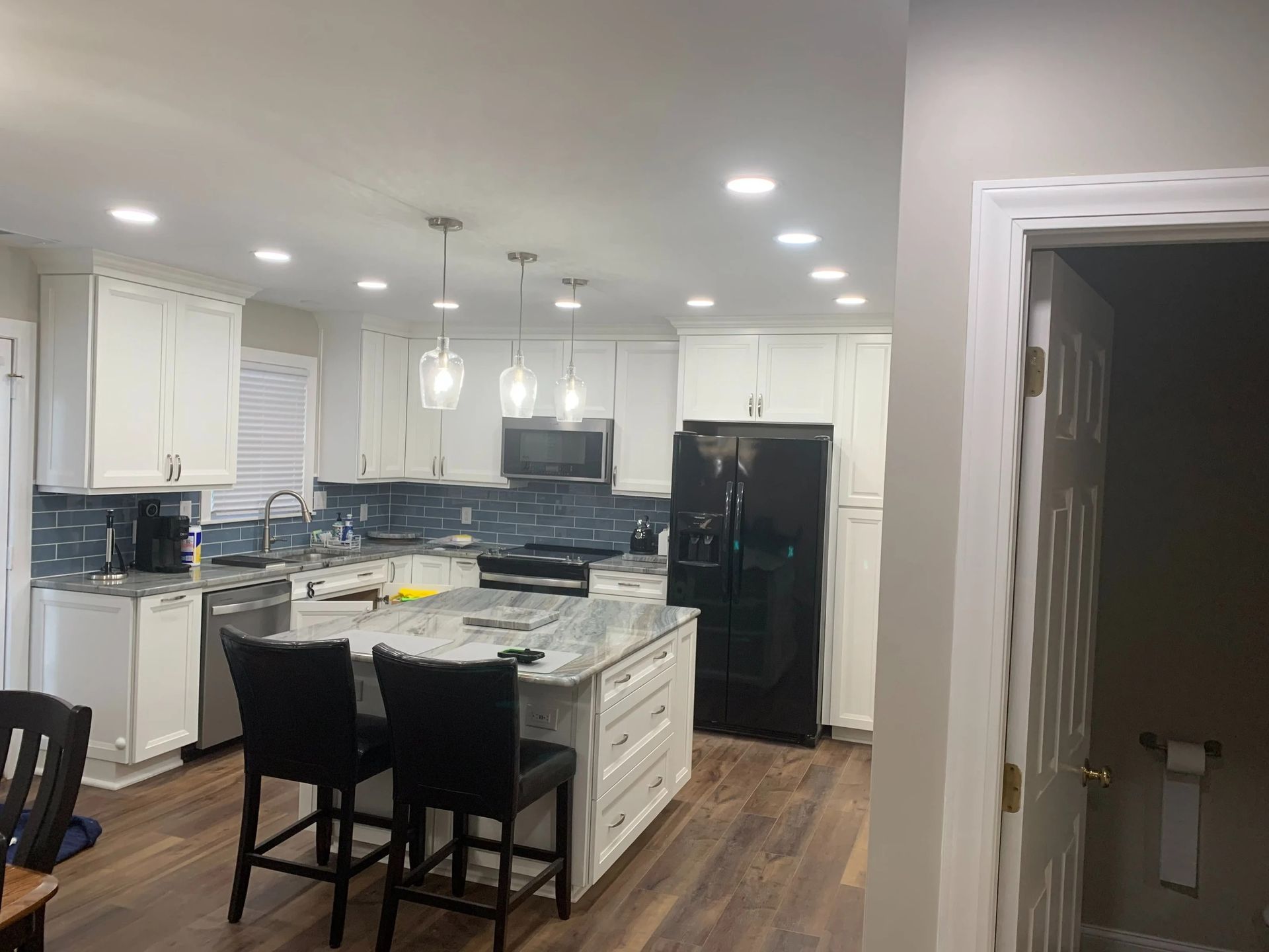 Bright modern kitchen with white cabinets, black island stools, and stainless steel appliances