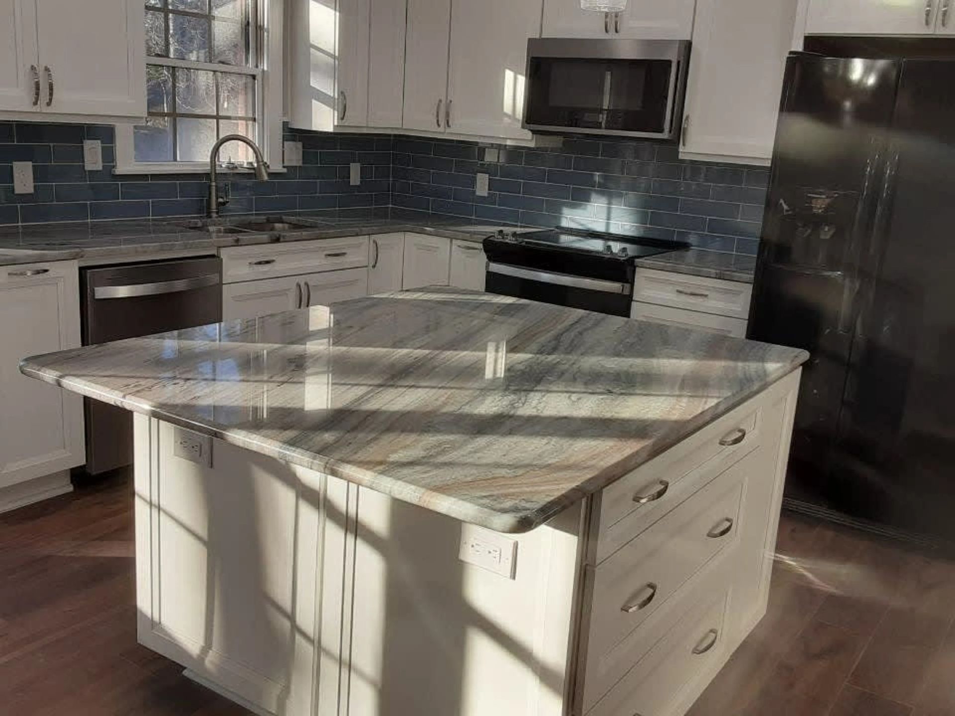 Modern kitchen with white cabinets, stainless appliances, blue tile backsplash, and a marble-top island.