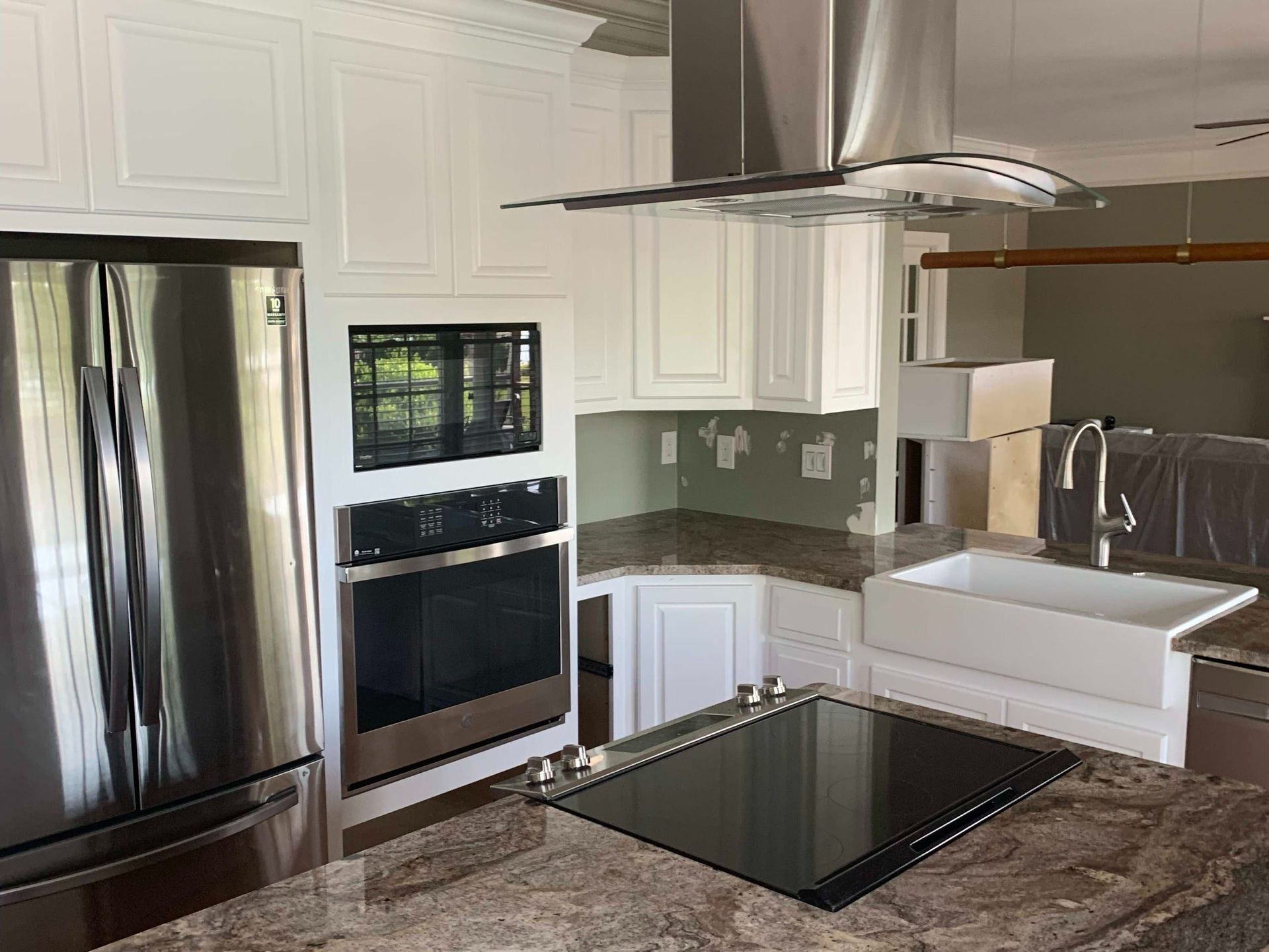 Modern kitchen with stainless steel appliances, white cabinets, black cooktop, and marble-patterned countertops