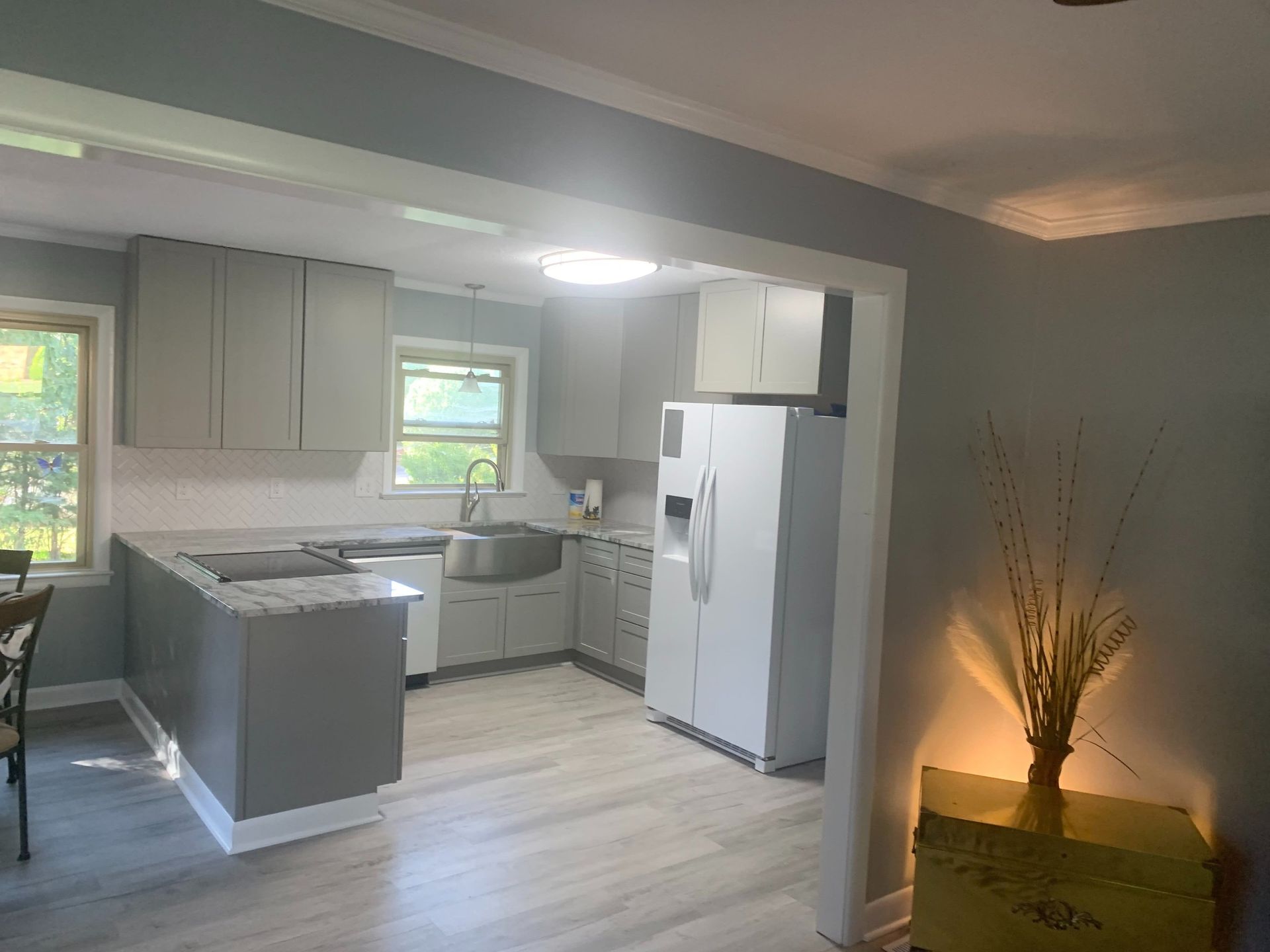 Bright, modern kitchen with white cabinets, island, refrigerator, and a lit decorative plant in the corner