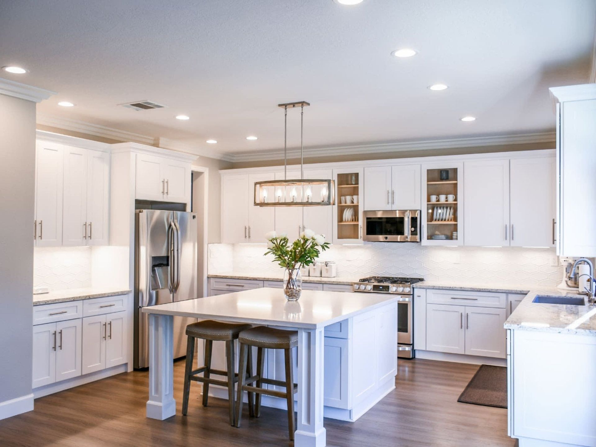 Bright white modern kitchen with island, stools, stainless fridge, and pendant light
