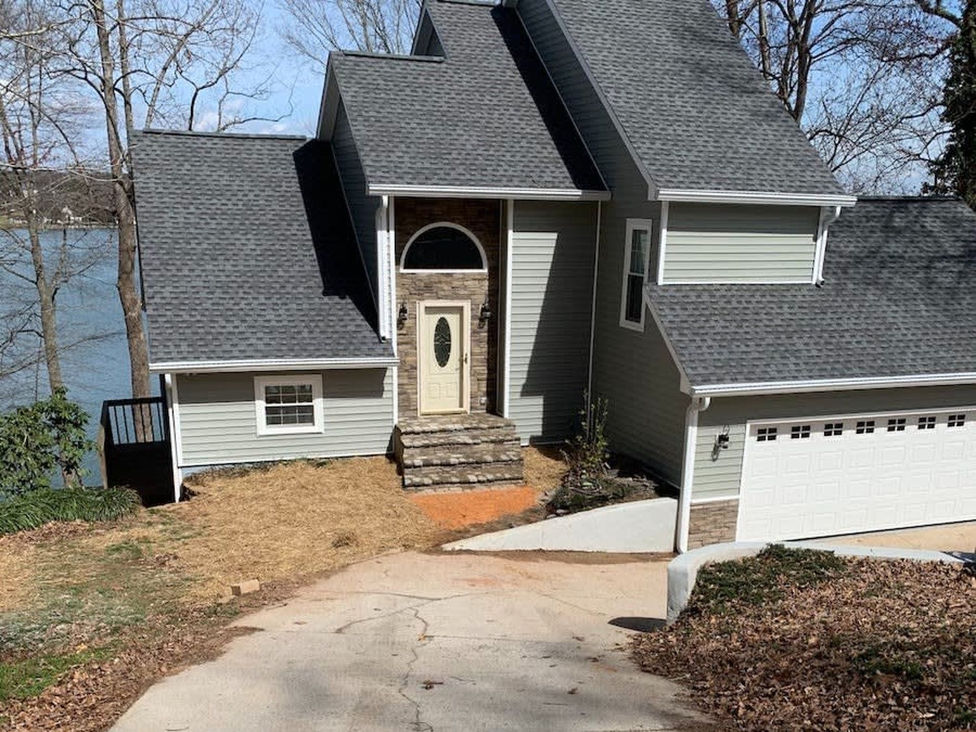 Suburban house with steep roof, front steps, driveway, and attached garage on a wooded lot.