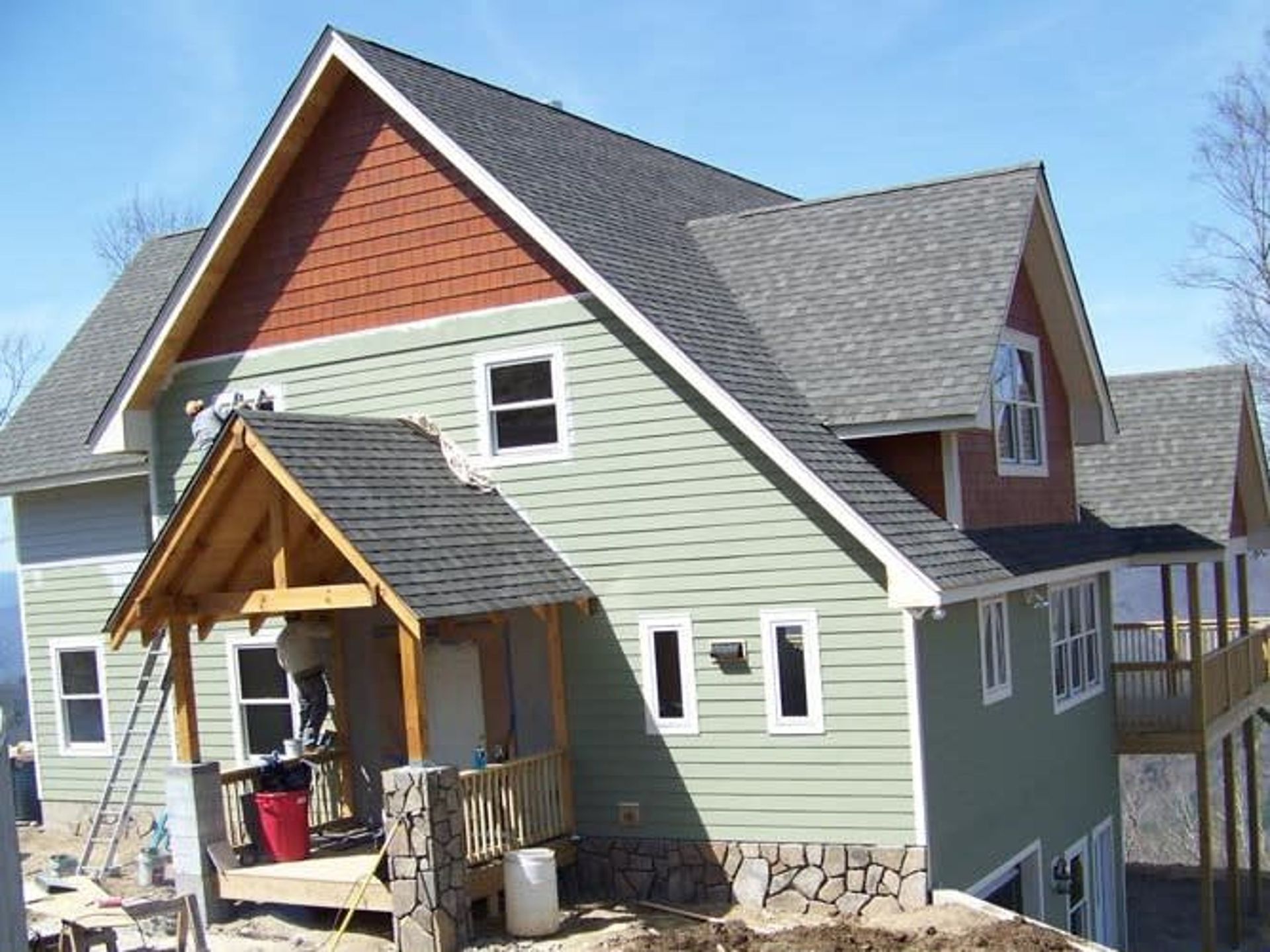 New house exterior with green siding, red gable, stone foundation, and a small covered porch
