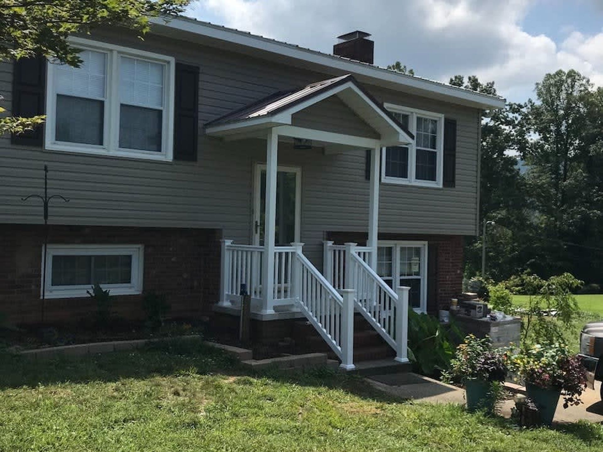 Suburban house exterior with white front porch, stairs, and landscaped yard in daylight