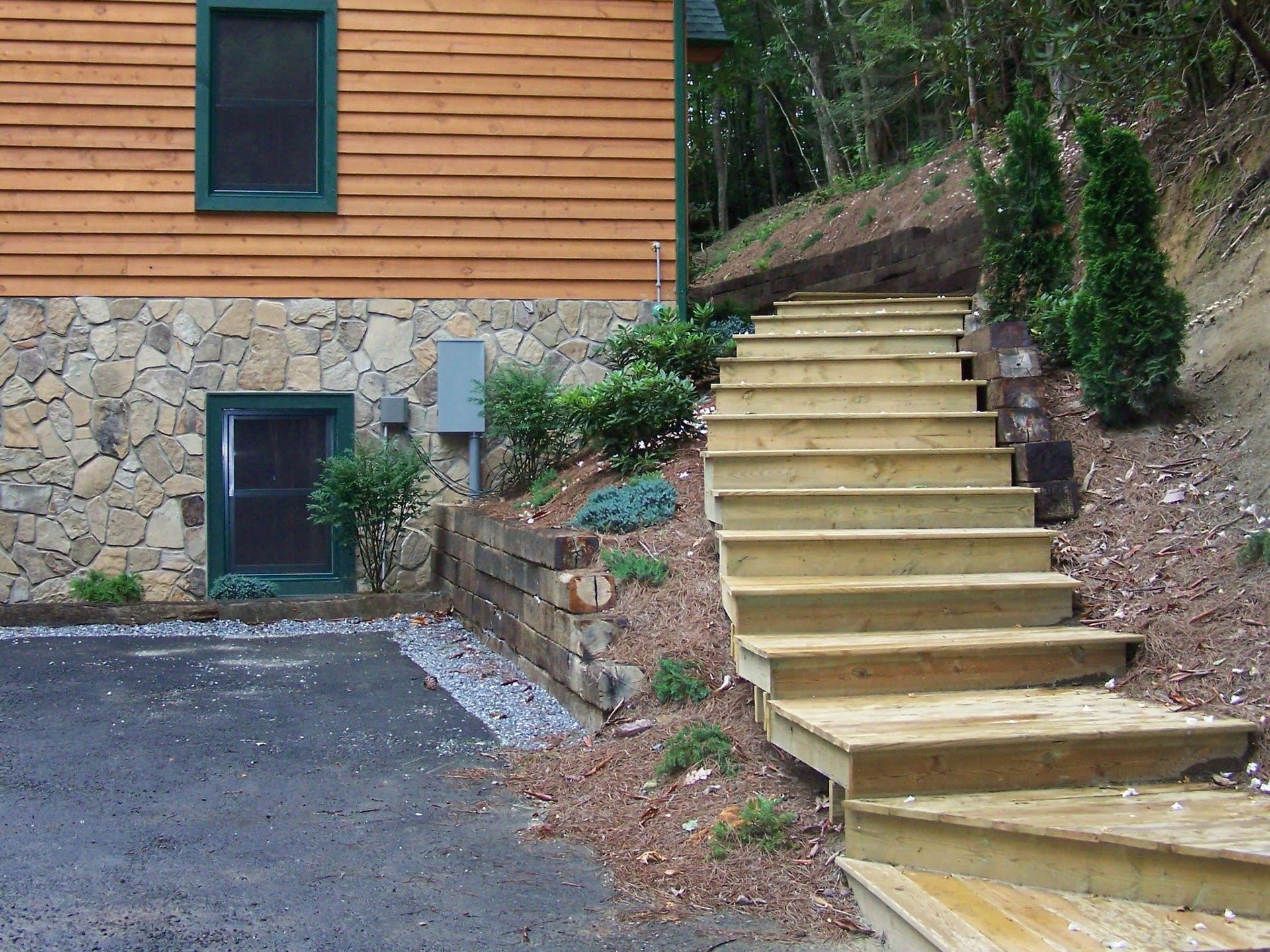 Exterior stairs beside a stone-and-wood house, leading up a wooded hillside.