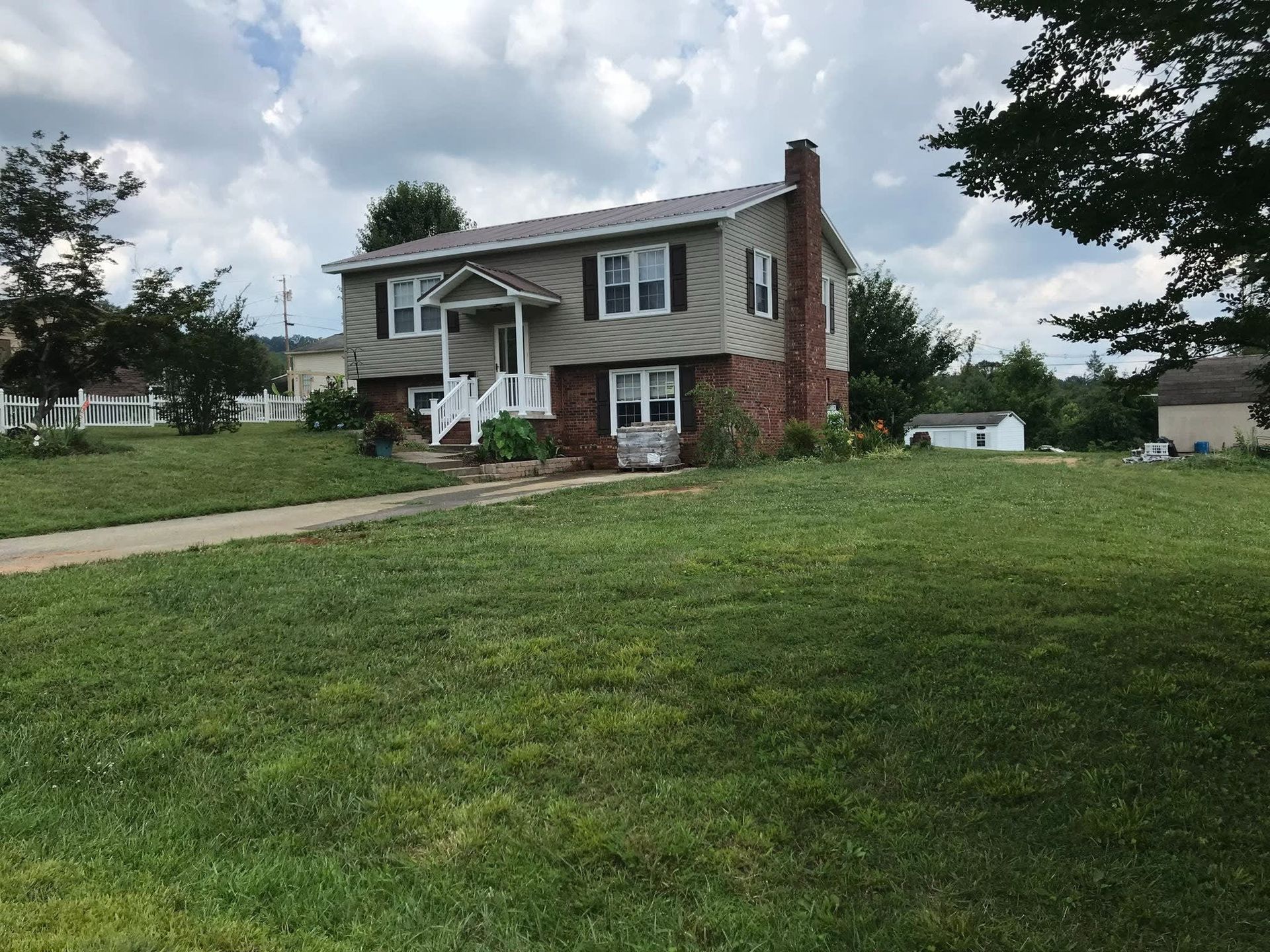 Suburban two-story house with a large green lawn, brick chimney, and cloudy sky.