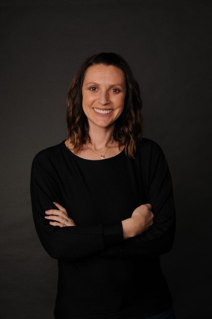 A woman in a black shirt is standing with her arms crossed and smiling.