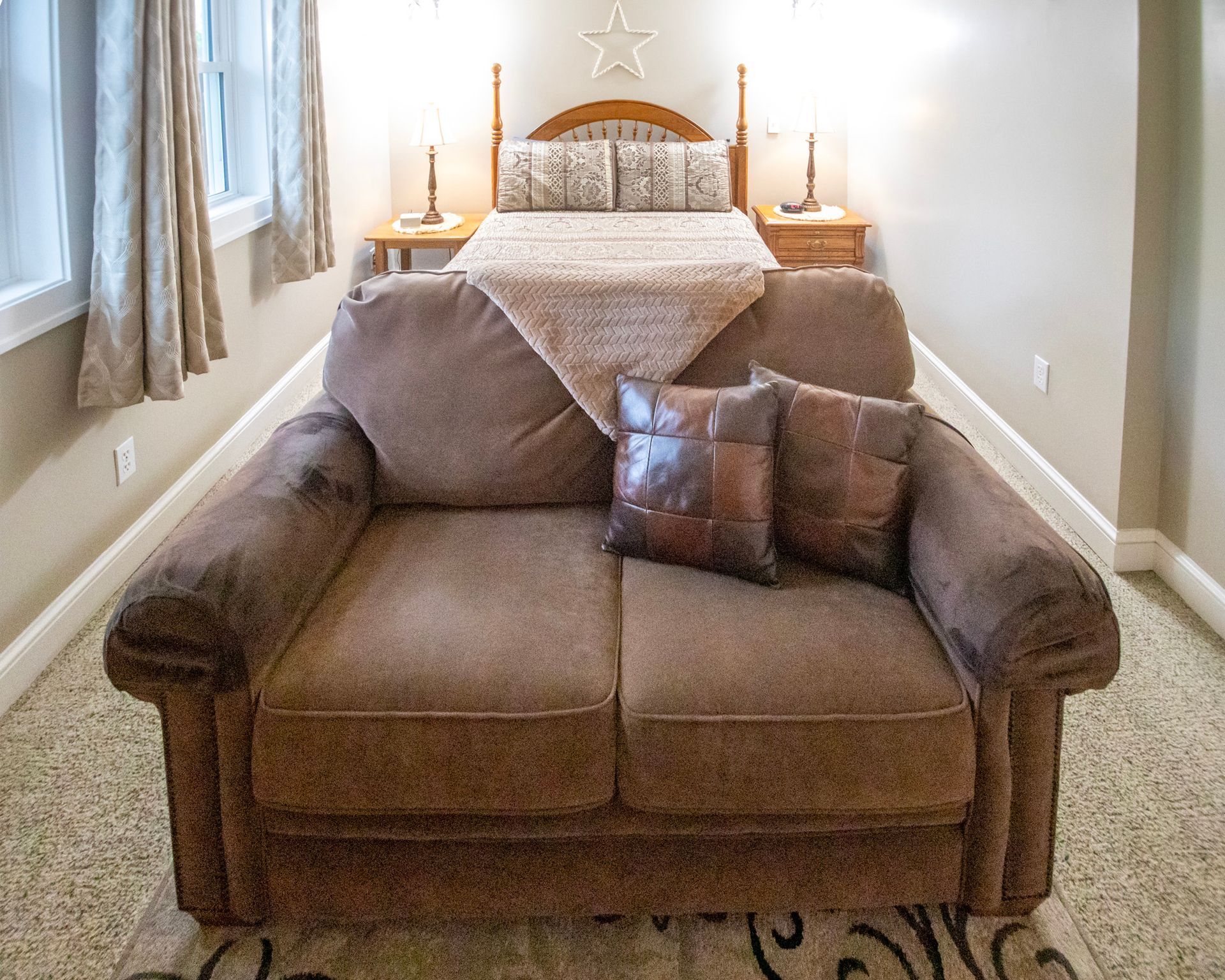 Brown loveseat in a bedroom with a bed, lamps, and a window.