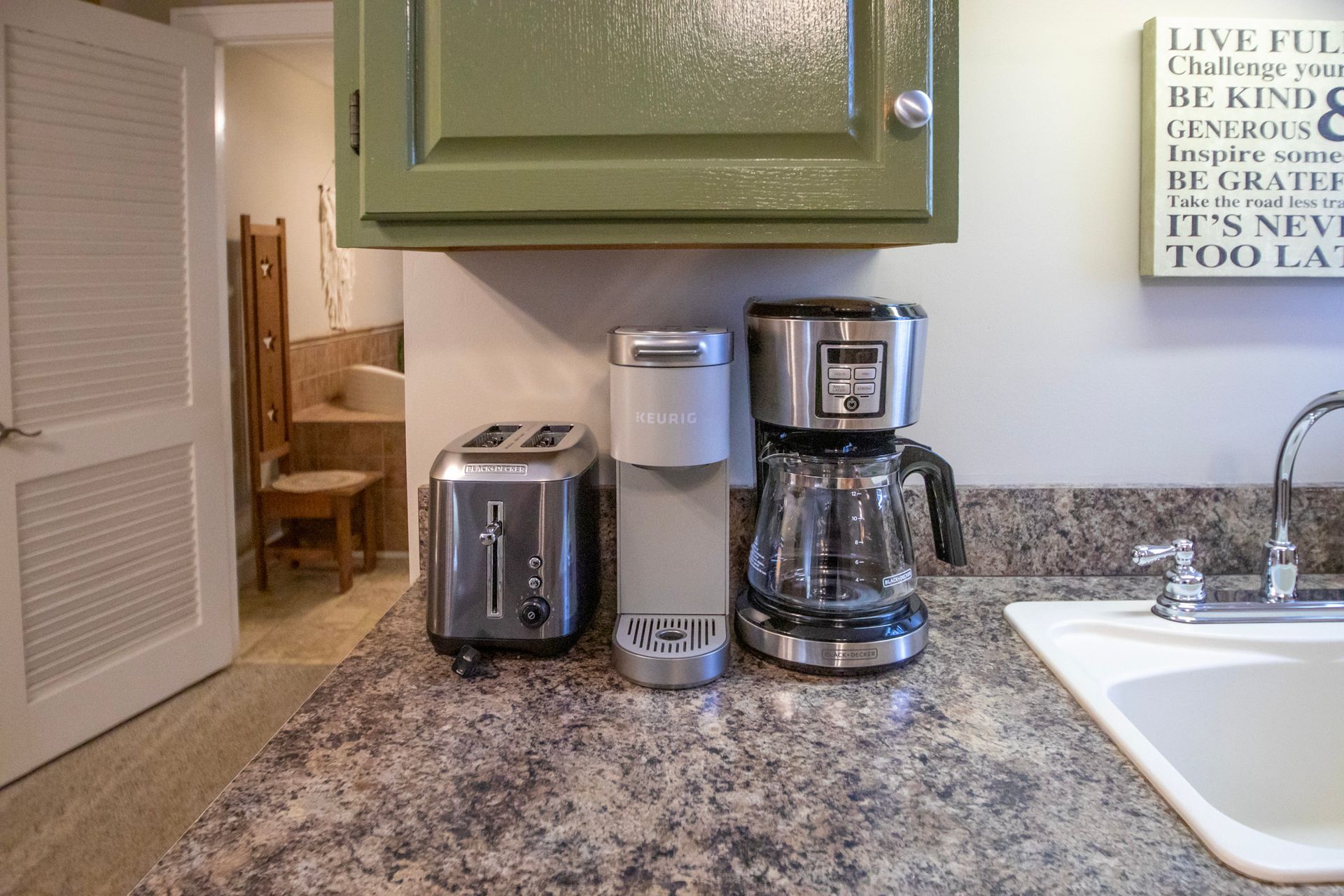 Kitchen counter with toaster, Keurig, coffee maker, and sink, under green cabinet.