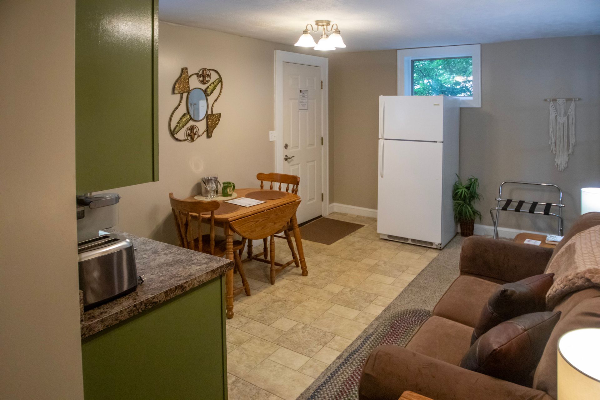 Small, furnished room with kitchen area, table, couch, refrigerator, and door.