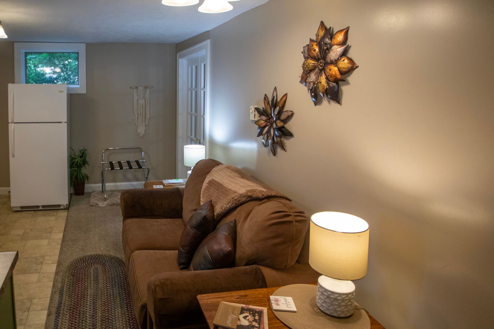 Living room with brown couch, lamps, and wall decor. Refrigerator visible.