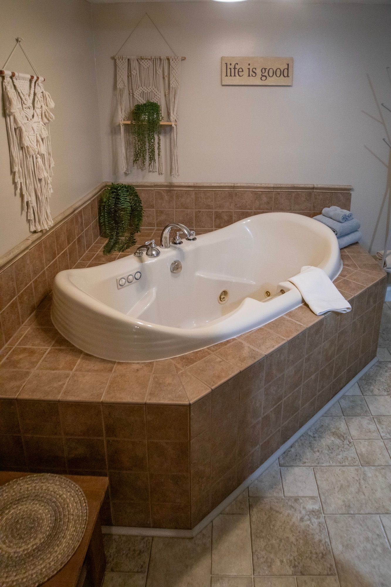 Corner jacuzzi tub in a tiled bathroom with decorative wall hangings.
