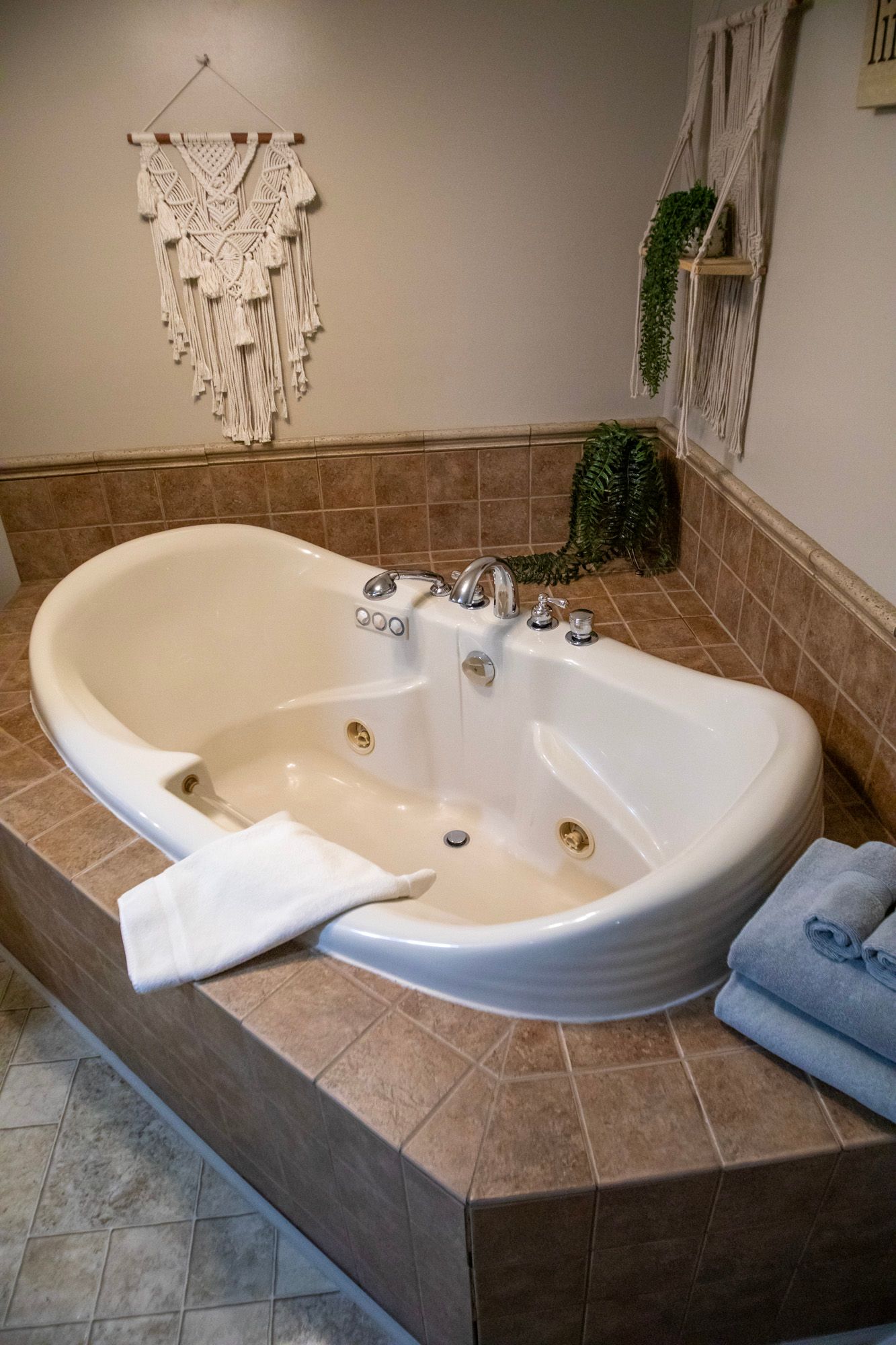 Built-in white bathtub with chrome fixtures, surrounded by brown tile. Light-colored walls and decor.