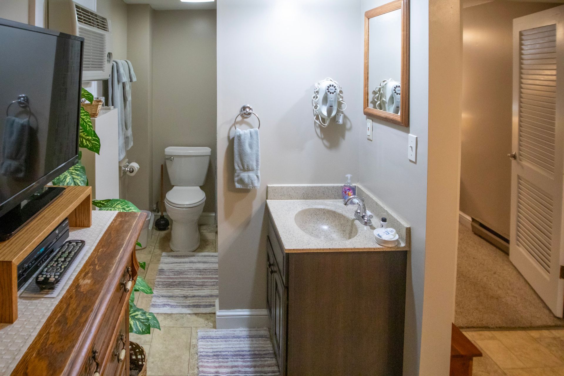 Bathroom with a toilet, vanity, and mirror; a doorway to the right.