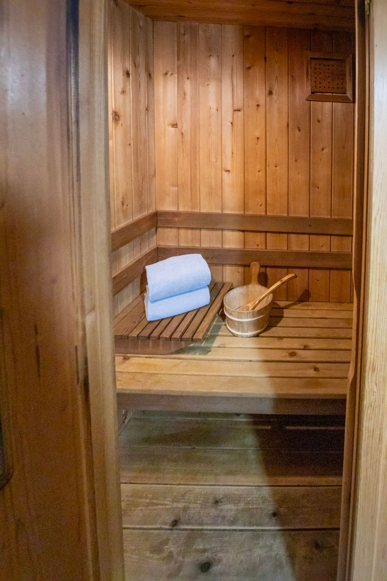 Wooden sauna interior with towels, bucket, and ladle on a bench.