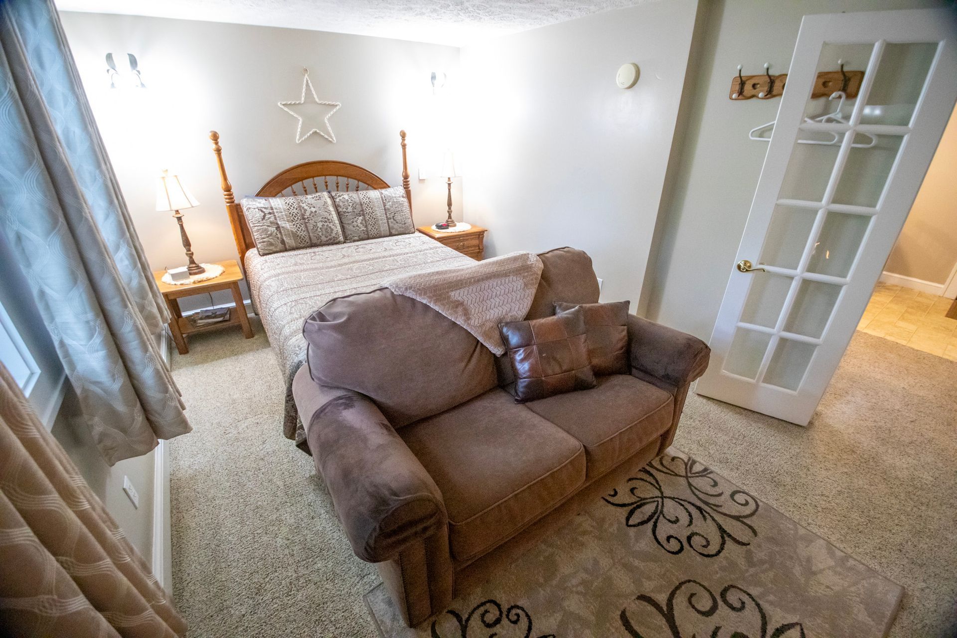Bedroom with a bed, small sofa, rug, and French doors. Neutral colors.