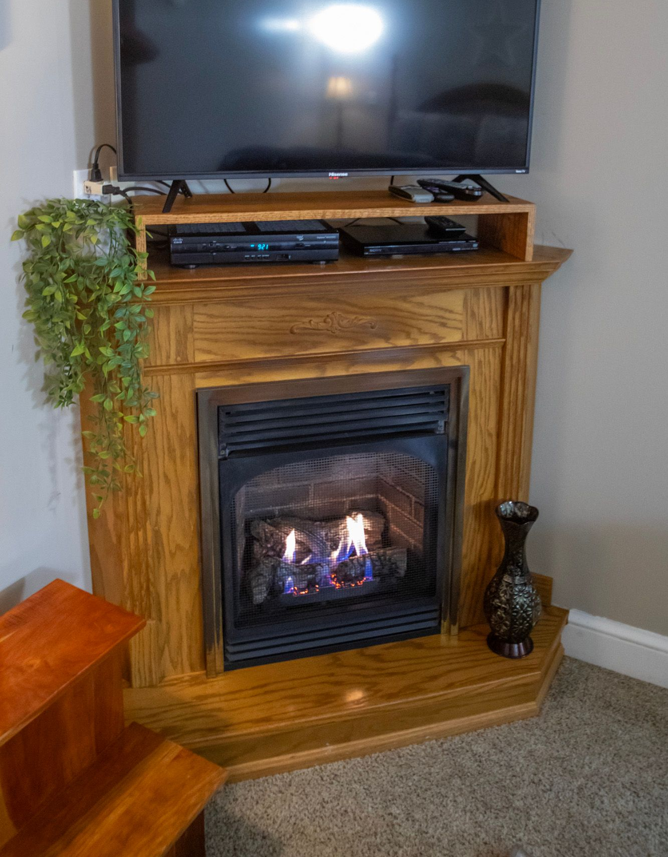 Wooden corner fireplace with burning flames, a TV above, and decorative accents.